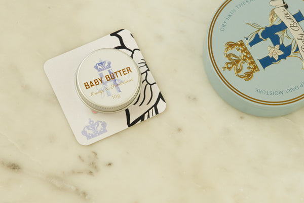 Baby Butter pocket-size tin in blue on a printed card beside the full-size blue tin