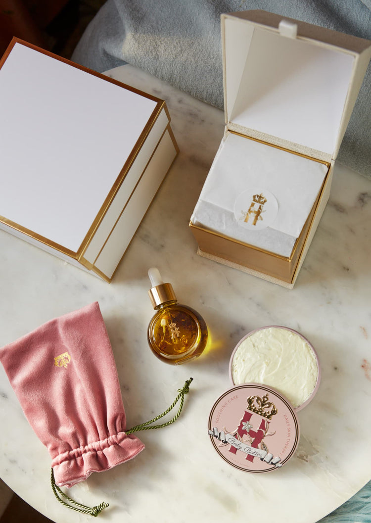 Open gift boxes, a serum bottle, a pink pouch and a Butter in Pink tin on a marble table