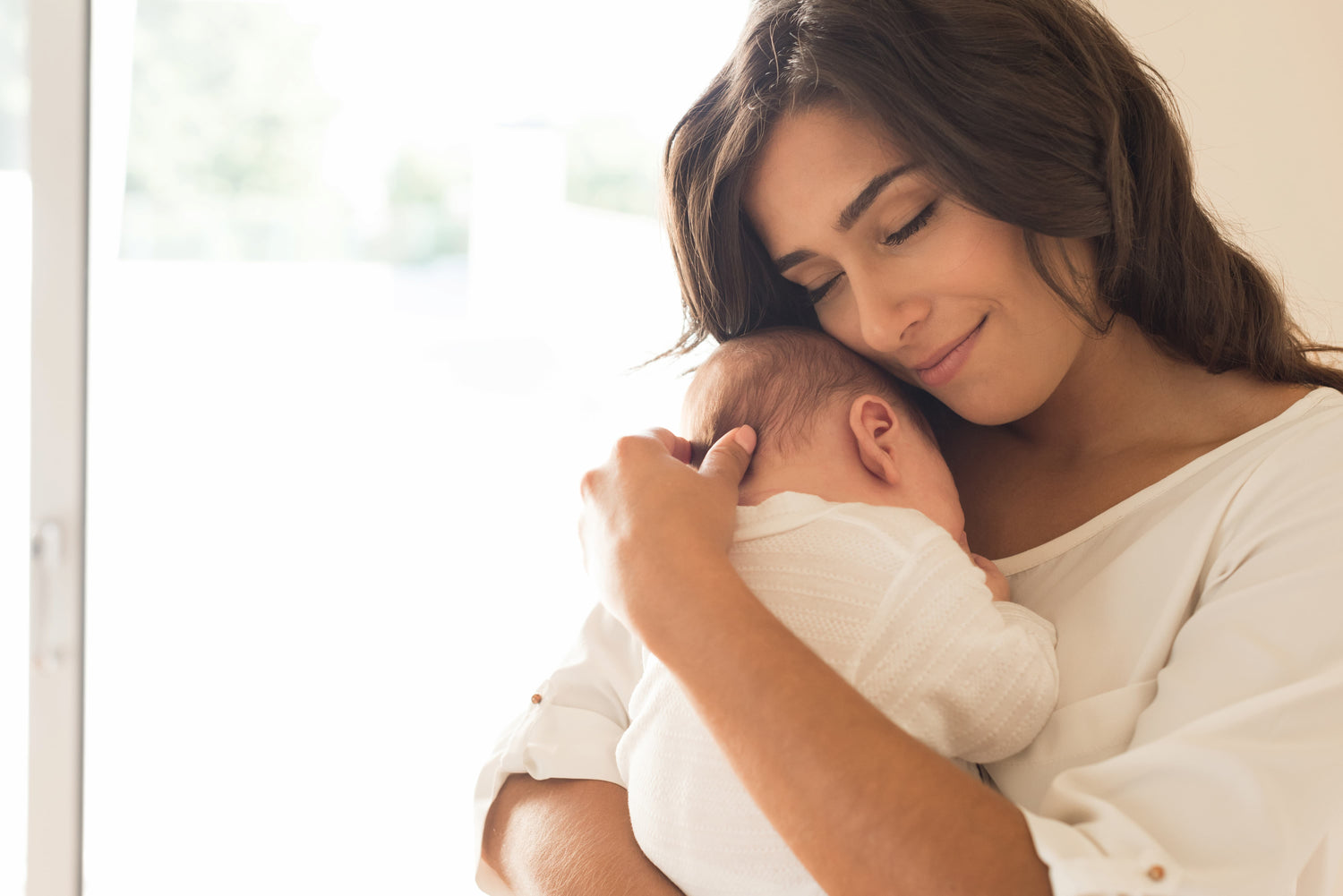 Young mother holding her baby close with a small smile on her lips.