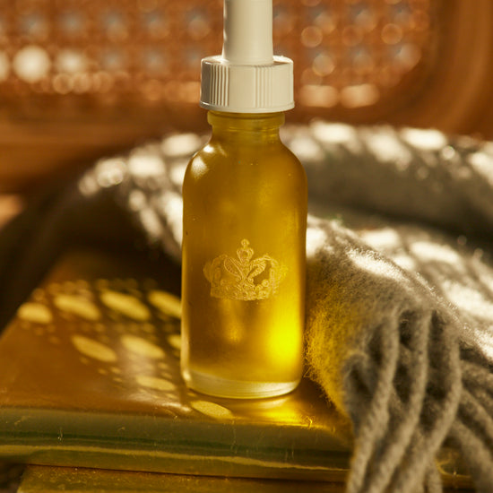 Serum bottle with a gold dropper on a golden surface beside a knitted throw and rattan