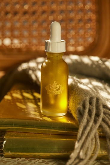 Serum bottle with a gold dropper on a golden surface beside a knitted throw and rattan
