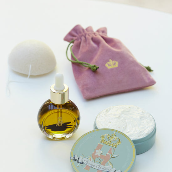Pink velvet pouch, a serum bottle, a konjac sponge and a Bump Butter tin on a white table