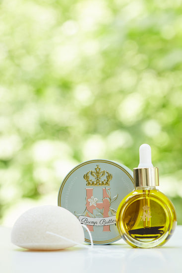 Bump Butter tin, a konjac sponge and a serum bottle in front of green foliage