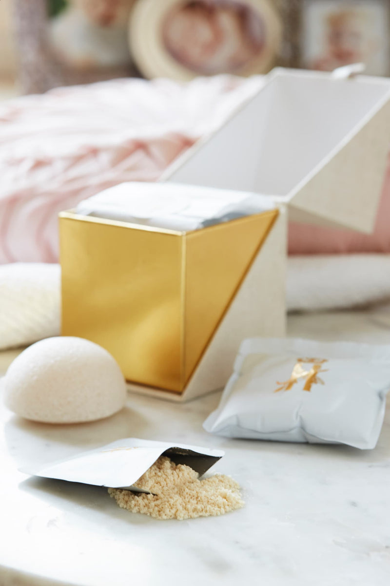 Open gold-lined ritual box with soak powder, a konjac sponge and a soak sachet on marble