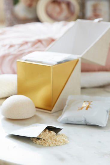 Open gold-lined ritual box with soak powder, a konjac sponge and a soak sachet on marble