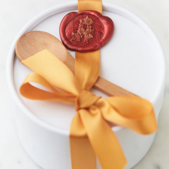 White round gift box tied with a gold ribbon and a red wax seal