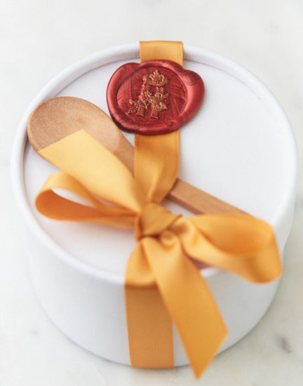 White round gift box tied with a gold ribbon and a red wax seal