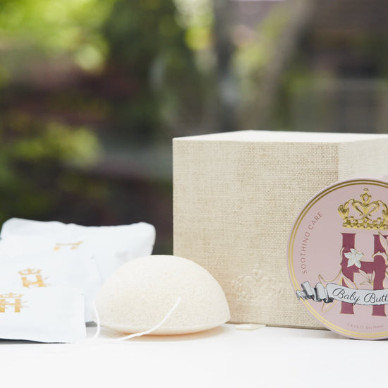 Linen gift box, soak sachets, a konjac sponge and a Butter in Pink tin in front of greenery