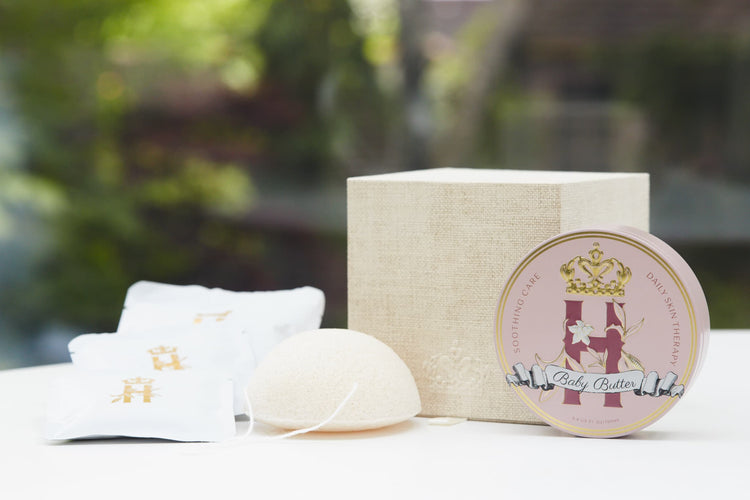 Linen gift box, soak sachets, a konjac sponge and a Butter in Pink tin in front of greenery