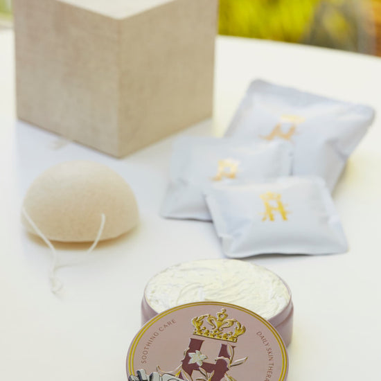 Linen gift box, soak sachets, a konjac sponge and a Butter in Pink tin on a white table