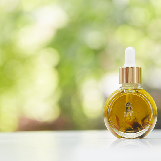Serum bottle with a gold dropper in front of blurred greenery, wide view