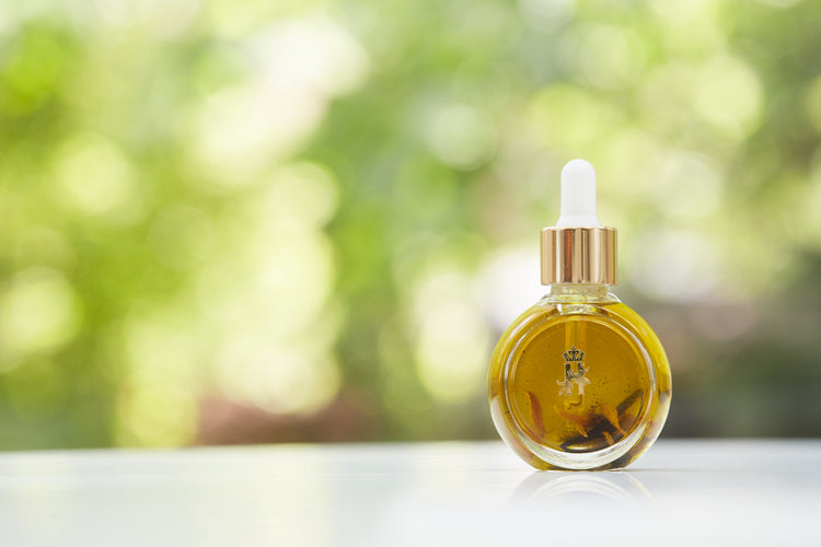 Serum bottle with a gold dropper in front of blurred greenery, wide view