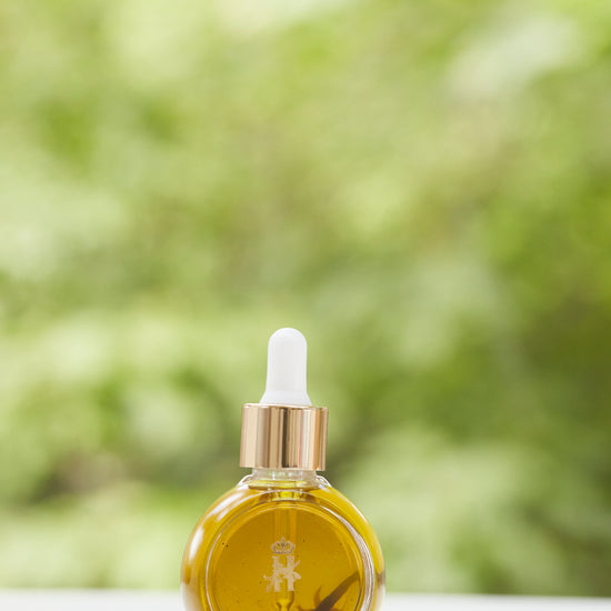 Serum bottle with a gold dropper in front of green foliage