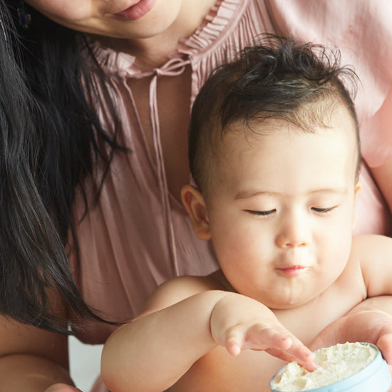 Mother holding her baby, who reaches into an open tin of Butter in Blue