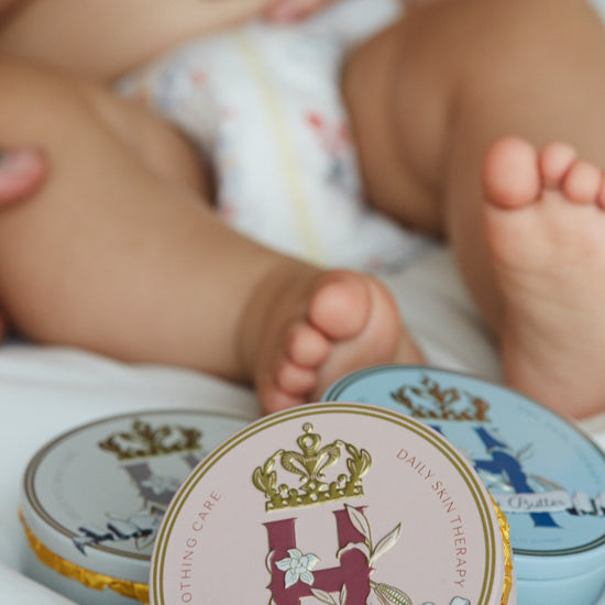 Baby's legs and feet in a diaper with Butter in Pink and Butter in Blue tins in front