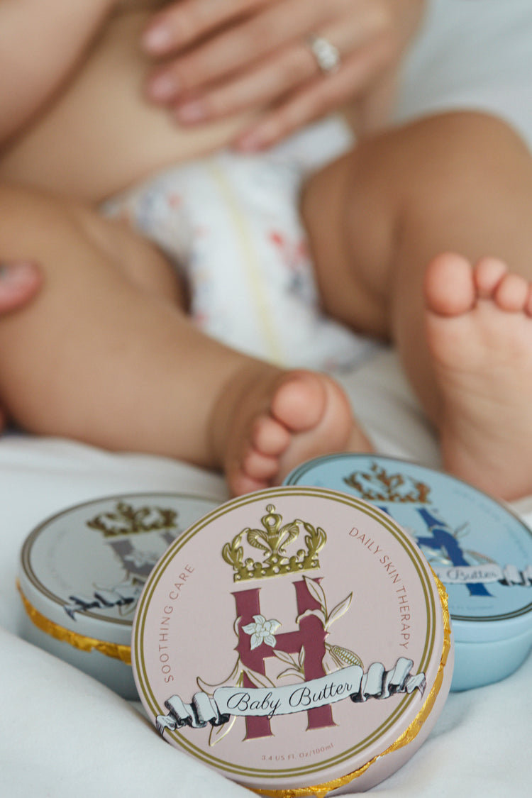 Baby's legs and feet in a diaper with Butter in Pink and Butter in Blue tins in front