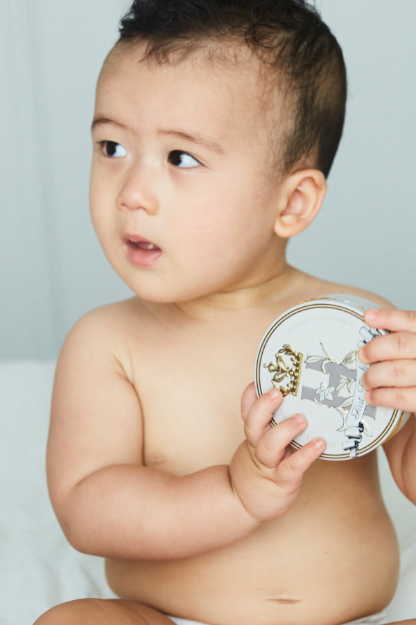 Baby holding a tin of Royal Heir Botanicals First Touch EWG verified Cocoa butter based butter for babies from day 1, the next best thing to Vernix