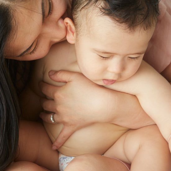 Mother kissing her baby, who sits bare-chested in a diaper in her arms