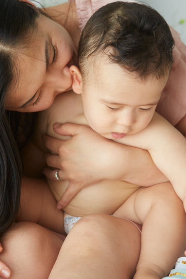 Mother kissing her baby, who sits bare-chested in a diaper in her arms