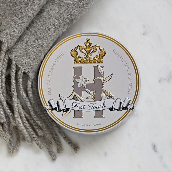 First Touch baby butter tin resting on white marble beside a grey wool scarf