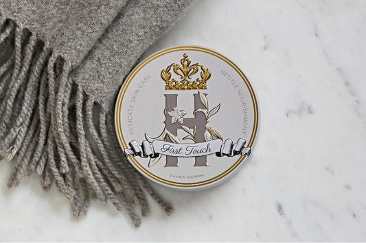 First Touch baby butter tin resting on white marble beside a grey wool scarf