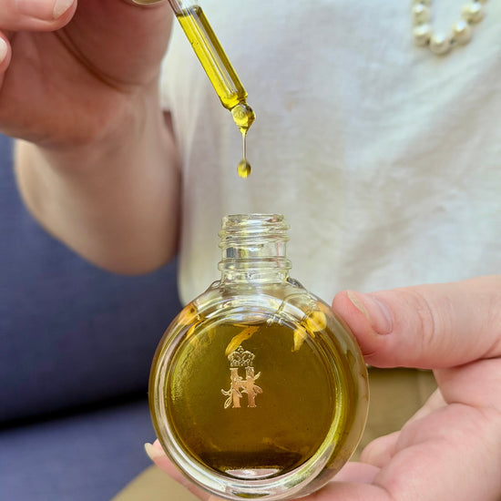 Hand squeezing a dropper over an open round glass serum bottle