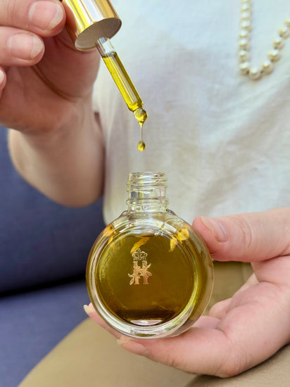 Hand squeezing a dropper over an open round glass serum bottle
