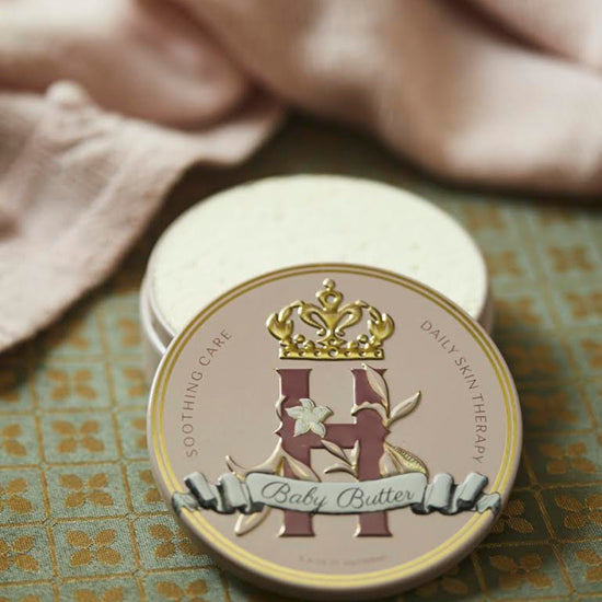 Butter in Pink tin on a patterned tile floor beside a pink knit blanket and an open tin