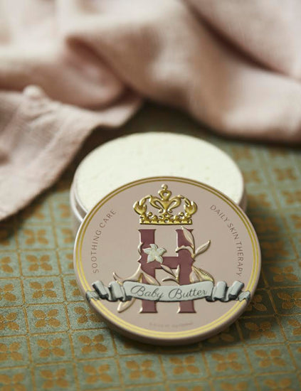 Butter in Pink tin on a patterned tile floor beside a pink knit blanket and an open tin