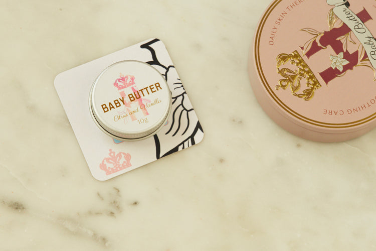 Baby Butter pocket-size tin in pink on a printed card beside the full-size pink tin