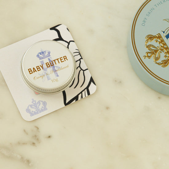 Baby Butter pocket-size tin in blue on a printed card beside the full-size blue tin
