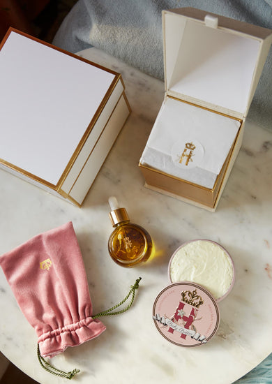 Open gift boxes, a serum bottle, a pink pouch and a Butter in Pink tin on a marble table