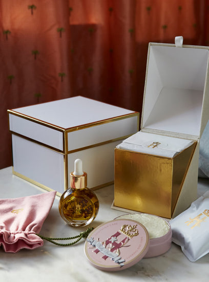 Open white and gold gift boxes with a serum bottle, a pink pouch and a pink tin