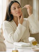 A woman in a white robe applying facial serum onto her face from a dropper