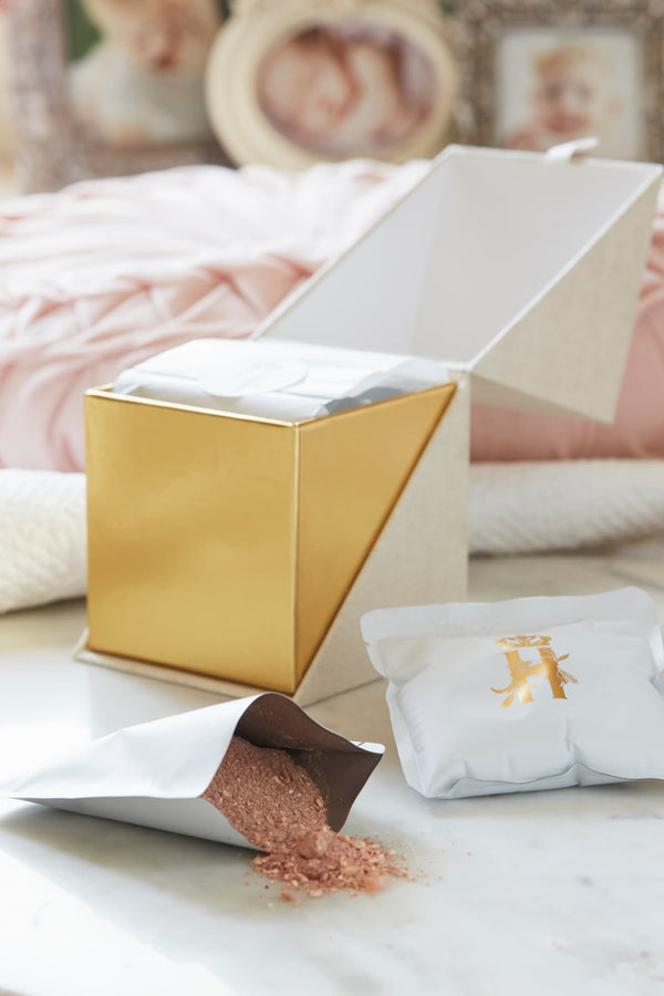 Open gold-lined ritual box with botanical soak powder spilling from a pouch and a soak sachet beside it