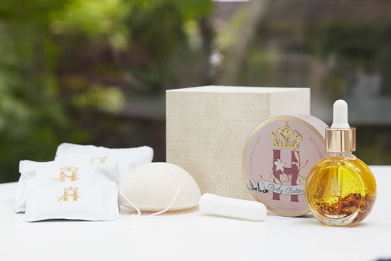 Linen gift box, soak sachets, a konjac sponge, a serum bottle and a pink tin on a white table