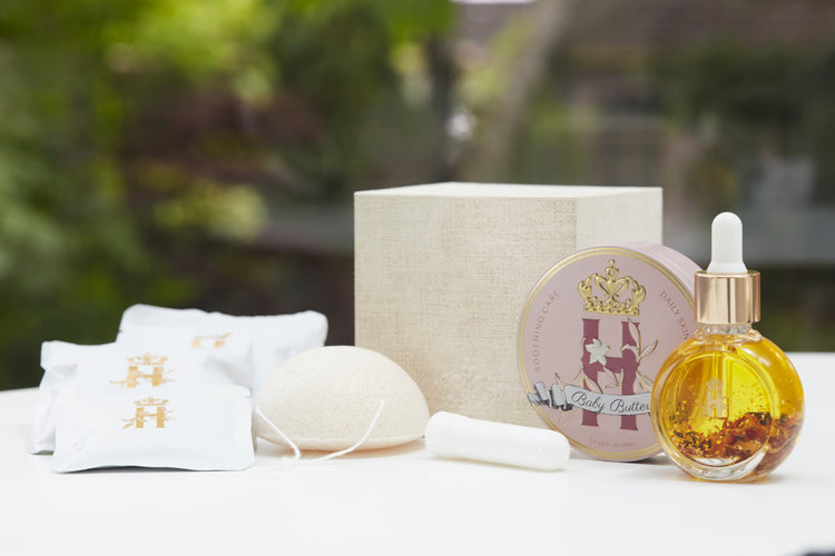 Linen gift box, soak sachets, a konjac sponge, a serum bottle and a pink tin on a white table