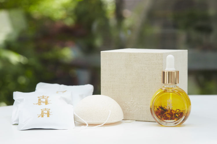 Linen gift box, soak sachets, a konjac sponge and a serum bottle with rose petals outdoors