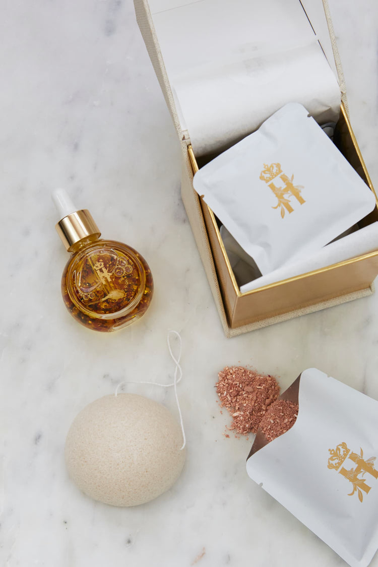 Serum bottle with rose petals, a konjac sponge and an open box with soak sachets on marble