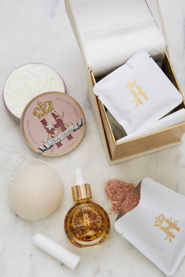 Butter in Pink tin, an open tin of butter, a serum bottle, a konjac sponge and an open box with soak sachets on marble