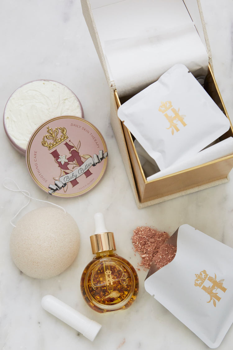 Butter in Pink tin, an open tin of butter, a serum bottle, a konjac sponge and an open box with soak sachets on marble