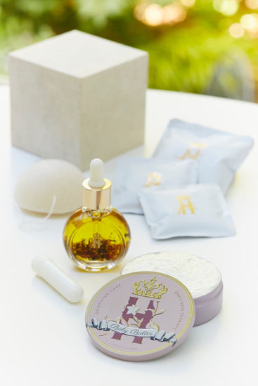 Linen gift box, soak sachets, a konjac sponge, a serum bottle and a Butter in Pink tin outdoors
