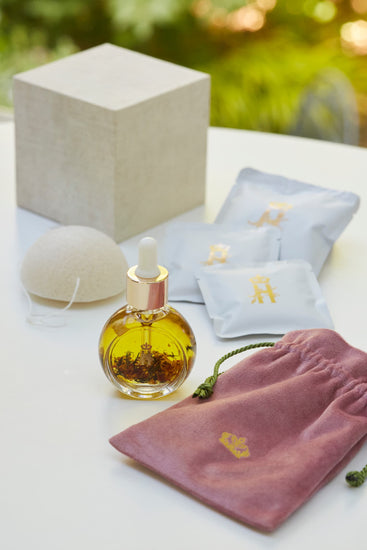Linen gift box, a konjac sponge, soak sachets, a serum bottle with rose petals and a mauve velvet pouch