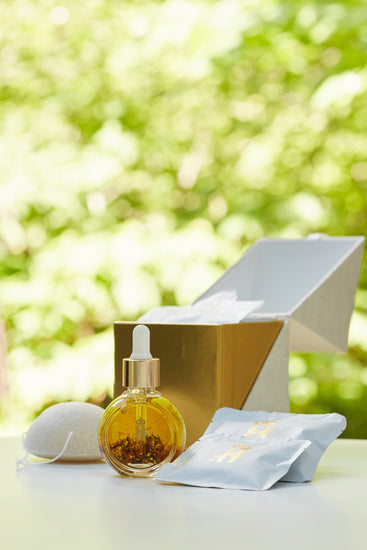 Serum bottle, a konjac sponge, soak sachets and an open gold box in sunlit greenery