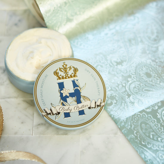 Butter in Blue tin with a gold crown beside an open tin of whipped butter on turquoise brocade