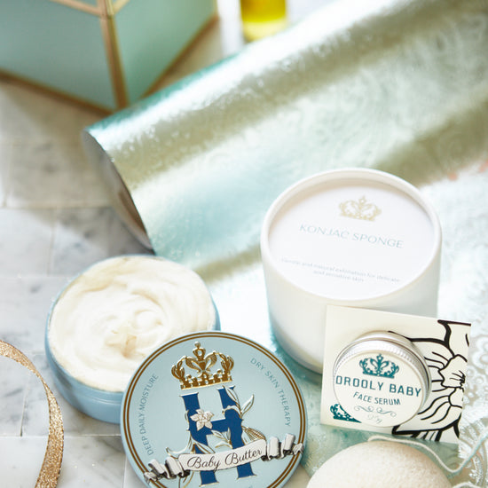 Butter in Blue tin with a konjac sponge, an open tin of butter and a serum bottle on a glass tray