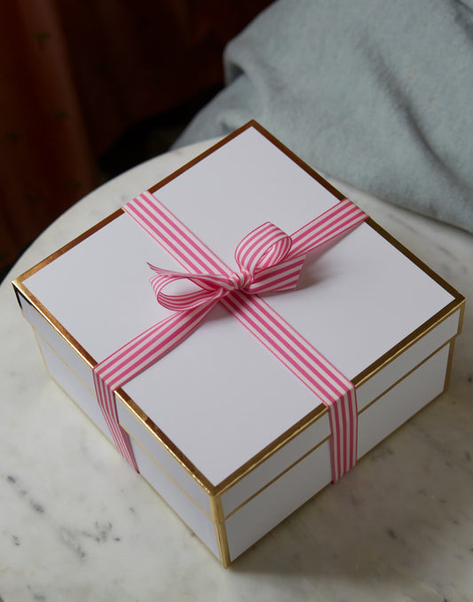 White gift box tied with a pink striped ribbon on marble