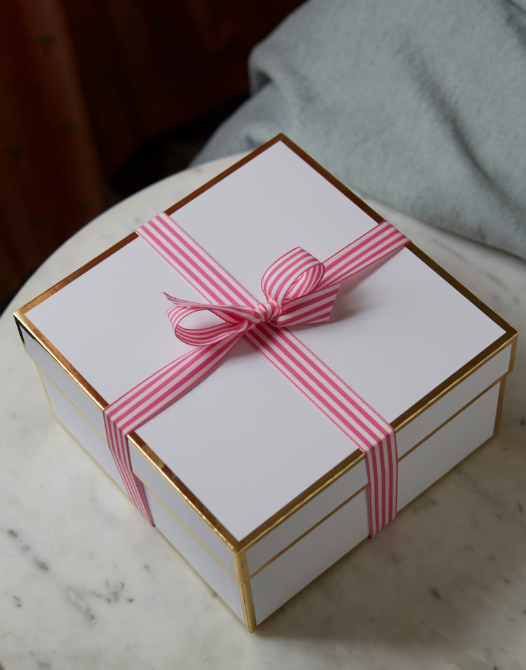 White gift box tied with a pink striped ribbon on marble