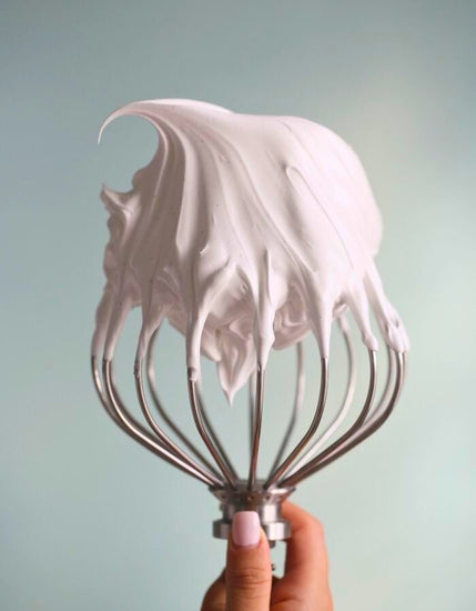 Hand holding a whisk lifted from pale-pink whipped butter