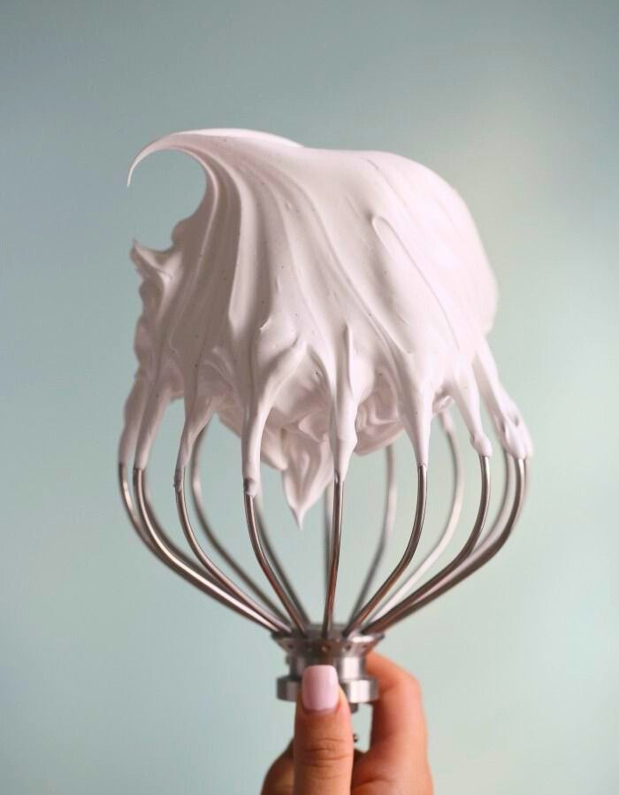Hand holding a whisk lifted from pale-pink whipped butter